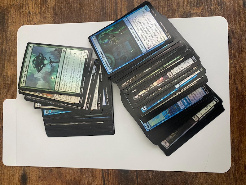 May include: Stacks of Magic: The Gathering trading cards, featuring various card designs and colors. The cards are arranged in two separate piles on a white surface. Some cards have text and illustrations.