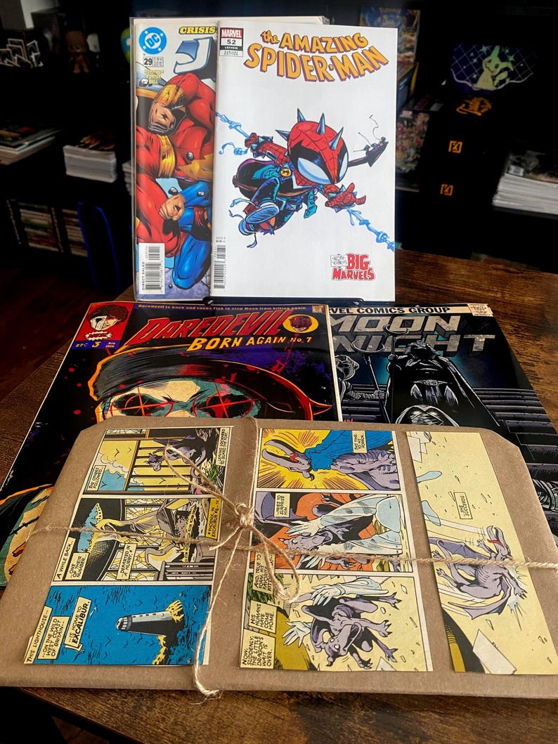 Pu&ograve; includere: Una collezione di fumetti tra cui The Amazing Spider-Man, Daredevil Born Again e Moon Knight, insieme a un pacchetto avvolto in carta marrone legato con spago, con vignette di fumetti stampate sulla superficie anteriore.