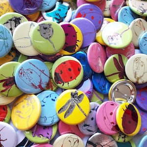 May include: A collection of colorful round buttons with various designs, including a dragonfly, a ladybug, a bird, and a mouse. The buttons are made of metal and have a shiny finish.