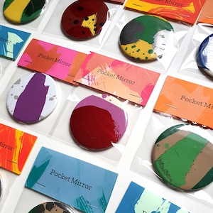 Puede incluir: Surtido de espejos de bolsillo coloridos con diseños abstractos. Cada espejo está empaquetado en una bolsa de plástico transparente con una tarjeta que dice "Pocket Mirror".