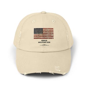 Può includere: Un berretto da baseball beige consumato con una bandiera americana vintage e il testo "Proud Military Kid" in nero.