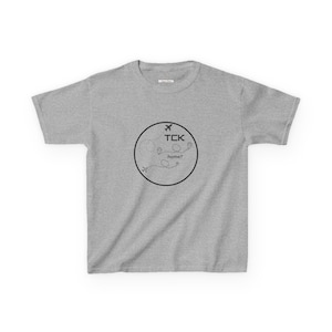 May include: Grey t-shirt with a black circle graphic featuring a plane, the text "TCK", and the words "home?"