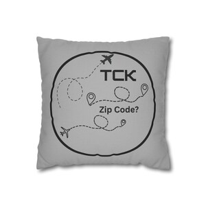 May include: Grey throw pillow with a black circle design. The circle features a plane, a map with dotted lines, and the text "TCK Zip Code?"