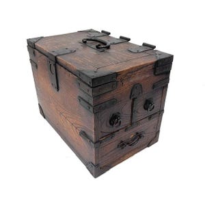 May include: A rectangular wooden chest with a dark brown finish, featuring black metal corner reinforcements, hinges, and latches. The chest includes a top handle, two small upper drawers with ring pulls, and one larger bottom drawer with a handle.