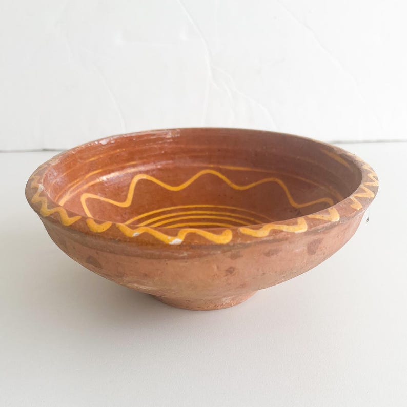 Pu&ograve; includere: Una ciotola color terracotta con un motivo ondulato giallo e bianco sul bordo e all'interno. La ciotola &egrave; rotonda e probabilmente utilizzata per servire cibo o come oggetto decorativo. Diametro di circa 20 cm.