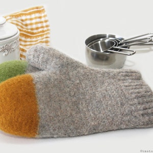 May include: A pair of gray, green, and yellow knitted oven mitts. The mitts are made of a thick, fuzzy material and have a striped design.