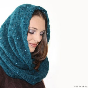 May include: A teal blue knitted cowl with sequins. The cowl is worn by a person with long brown hair.