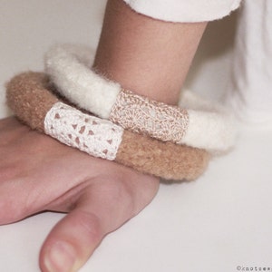 May include: Two crocheted bracelets on a person's wrist. The top bracelet is white with a brown crocheted design. The bottom bracelet is brown with a white crocheted design.
