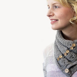 May include: A woman wearing a gray knitted scarf with wooden buttons. The scarf is folded over and has a textured pattern.
