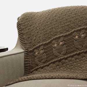 May include: A brown crocheted throw blanket with a woven owl design. The blanket is draped over a beige armchair.