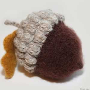 May include: A crocheted acorn with a brown felt bottom and a yellow felt cap. The acorn is a handmade craft item.