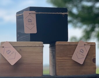 May include: Three wooden boxes with a natural wood finish, one painted black. Each box has a small brown tag with the text "It's All Wood" and a mountain logo.