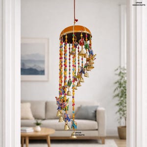 May include: A decorative hanging mobile featuring a golden-brown dome with a dark brown trim. Colorful beaded strands cascade down, adorned with small bells and painted figurines of elephants and people. The mobile is suspended from a red cord.