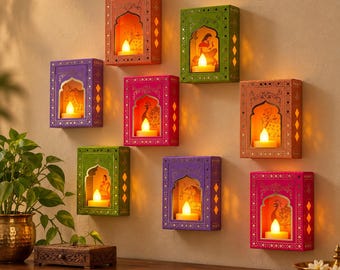May include: Eight rectangular wall-mounted candle holders in various colors including orange, green, purple, pink, and peach. Each holder features an arched cutout containing a glowing LED tea light and intricate patterns on the frame.