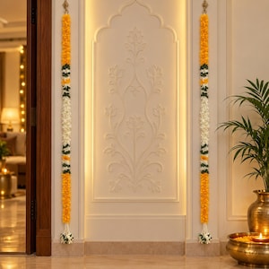 May include: Two long vertical floral garlands hanging on either side of a wall panel. Each garland features alternating sections of bright yellow marigold-like flowers, dark green leaves, and white jasmine-like blossoms, ending in a white floral tassel.