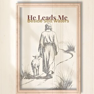Può includere: Opera d'arte incorniciata con un disegno di una figura in una veste che cammina con un agnello. Il testo "He Leads Me Beside Still Waters" è sopra le figure. La cornice è di colore legno chiaro.