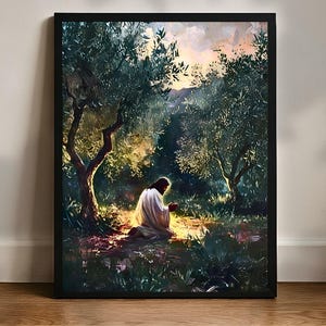 Puede incluir: Una impresión artística enmarcada representa una figura con túnica blanca arrodillada en una arboleda de olivos iluminada por el sol. La obra presenta un paisaje sereno con iluminación suave y una sensación de paz, enmarcada en un borde negro.