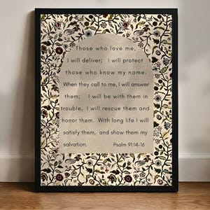 Könnte beinhalten: Gerahmter Druck mit einem Zitat aus Psalm 91:14-16. Der Text befindet sich auf einem hellbeigen Hintergrund mit einem dekorativen floralen Rand in Schwarz, Burgunderrot und Creme. Der Rahmen ist schwarz, und der Druck befindet sich auf einer Holzoberfläche.