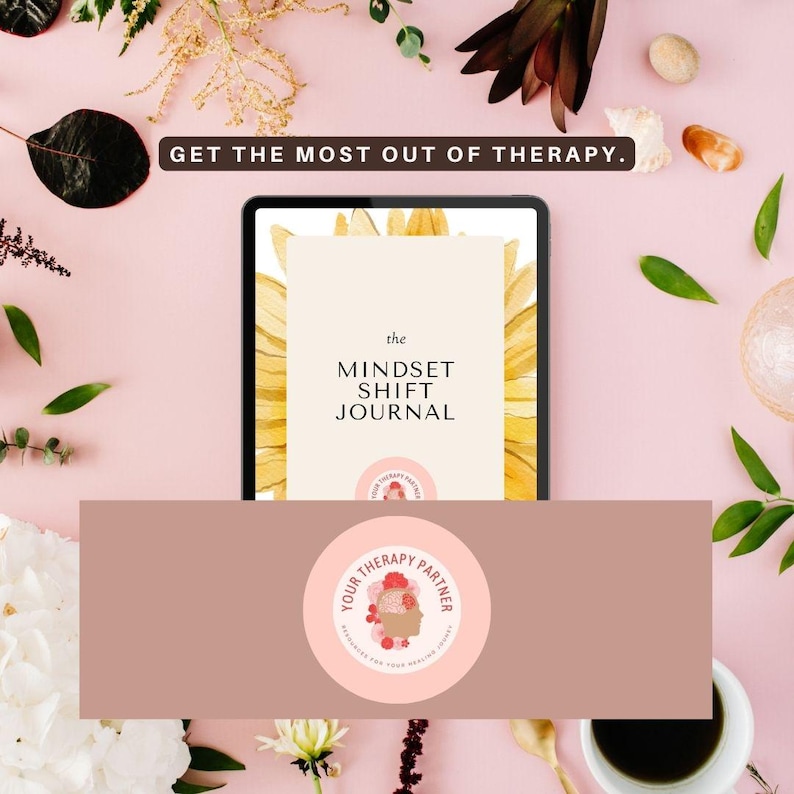 May include: A pink and brown digital tablet with a sunflower graphic on the screen. The text on the screen reads "the MINDSET SHIFT JOURNAL". The tablet is on a pink surface with flowers and a white cup.