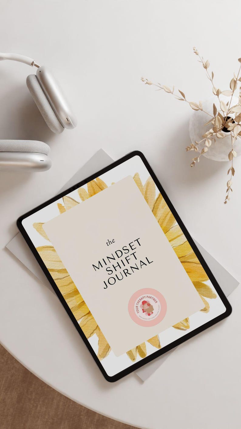 May include: A digital tablet displaying a journal cover with a watercolor sunflower design. The cover text reads "the MINDSET SHIFT JOURNAL" and features a pink circle with the text "YOUR THERAPY PARTNER".