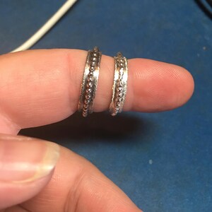 Pu&ograve; includere: Due anelli d'argento con un design a perline sono mostrati su un dito. Gli anelli hanno una fascia strutturata con una fila di piccole perline in rilievo lungo il centro. Sono gioielli.