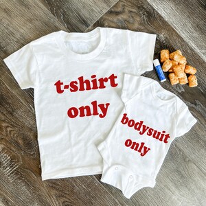 May include: Two white shirts with red text. The larger shirt says "t-shirt only" and the smaller shirt says "bodysuit only".