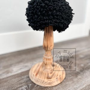May include: Black crocheted hat on a wooden stand. The hat is made of yarn and has a fluffy texture. The stand is made of wood and has a simple design.