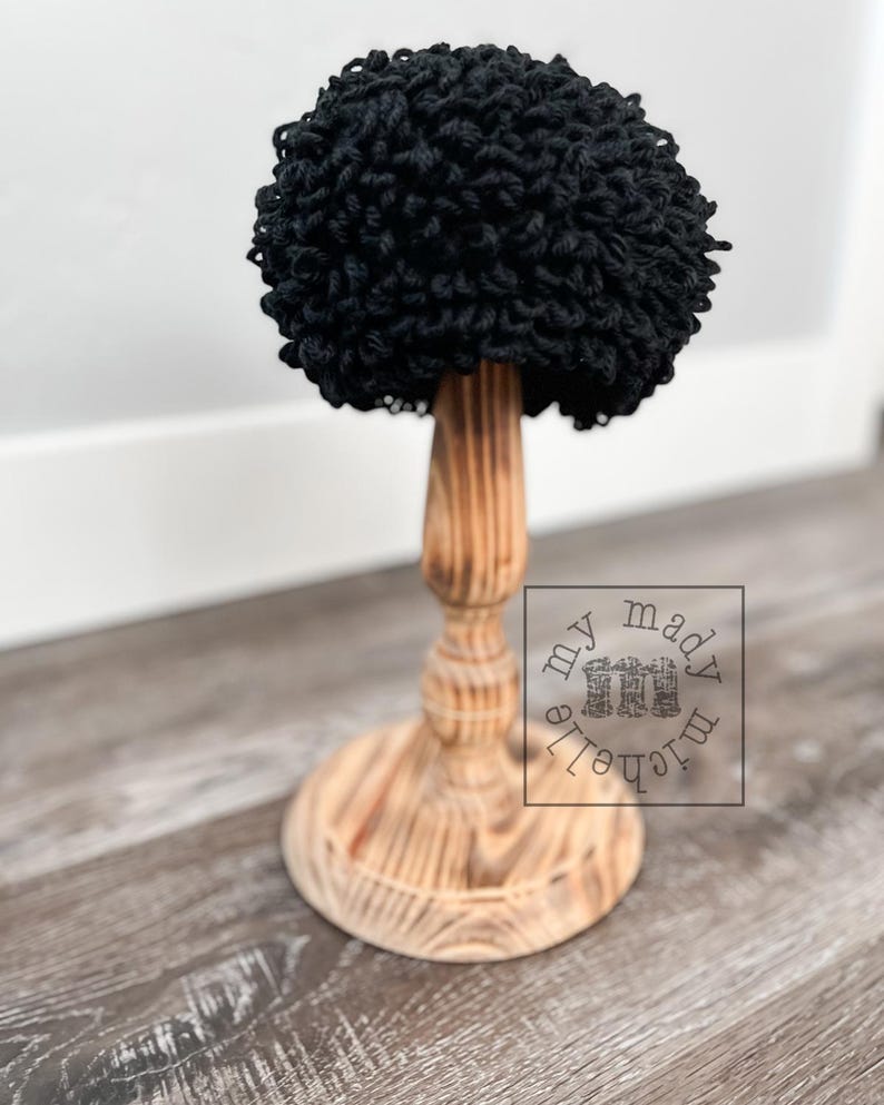May include: Black crocheted hat on a wooden stand. The hat is made of yarn and has a fluffy texture. The stand is made of wood and has a simple design.