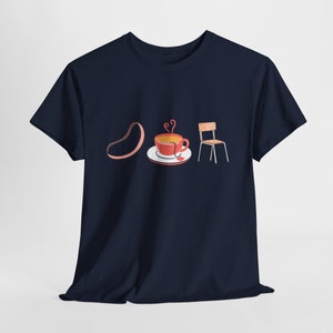Peut inclure: T-shirt bleu marine avec une illustration fantaisiste d'un haricot, d'une tasse de thé fumante et d'une petite chaise. Le design utilise des couleurs douces, créant une esthétique chaleureuse. Le t-shirt est en matière douce.