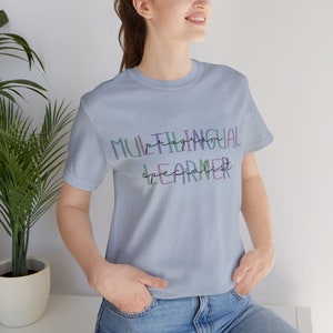 Op de afbeelding: Een lichtblauw t-shirt met de tekst "Multilingual Program Learner Specialist" in kleurrijke, handgeschreven letters.