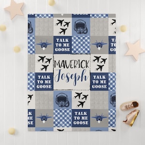 Puede incluir: Una manta para bebé azul y gris con un diseño de patchwork. La manta presenta un casco de piloto, aviones y el texto "Talk to me Goose" y "Maverick Joseph".