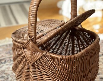 May include: A brown wicker picnic basket with a handle and hinged lid. The basket is made of woven wicker and has a classic design, perfect for outdoor dining or storage.
