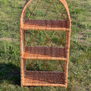 May include: A three-tiered wicker shelf with an arched top. The shelf is made of natural woven wicker and has a light brown color.
