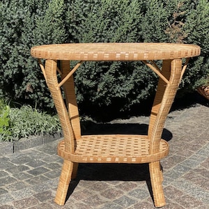 May include: A light brown wicker side table with a round top and a lower shelf. The table has four legs and is made of woven wicker material. The table is approximately 28 inches tall.