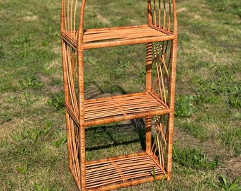 May include: A three-tiered wicker shelf with an arched top. The shelf is made of natural brown wicker and has a rustic, farmhouse style.