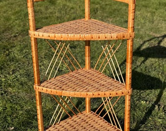 May include: A three-tiered corner shelf made of woven wicker. The shelf is light brown and has a natural finish. It is perfect for displaying plants, books, or other decorative items.