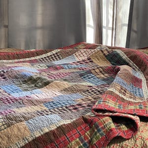 May include: A patchwork quilt with a red, brown, blue and green plaid pattern. The quilt is folded over a bed with a floral patterned bedspread.