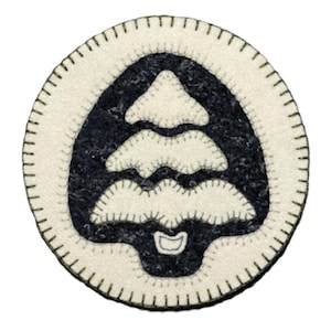 May include: Circular, off-white rug with a black tree design in the center. The tree has a stylized shape with multiple layers. The rug's edge is finished with a stitched border. The design is simple and rustic.