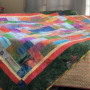 May include: A colourful patchwork quilt with a green, red and cream border. The quilt is made of various fabrics with floral and geometric patterns.