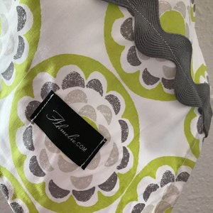 May include: A white fabric with a green and gray floral pattern. The fabric has a gray scalloped edge and a black label with the text "Abloomie.com".