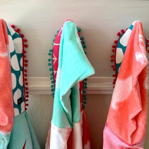May include: Three hooded towels hanging on hooks. The towels are made of a soft, absorbent material and feature a variety of colourful patterns. The towels are perfect for drying off after a bath or shower.