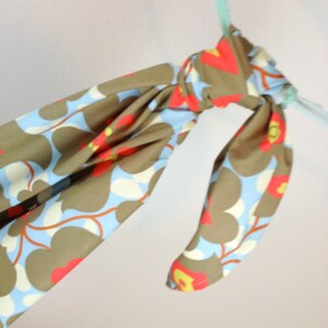 May include: A brown and blue fabric scarf with a floral pattern. The scarf is tied in a knot and hanging from a light blue ribbon.