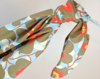 May include: A brown and blue fabric scarf with a floral pattern. The scarf is tied in a knot and hanging from a light blue ribbon.