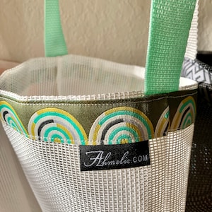 May include: White mesh tote bag with green straps and a green, black, and white patterned trim. The bag has a black label with the text "Almelia.com".
