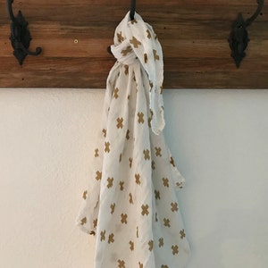 May include: A white scarf with a gold cross pattern hangs on a wooden hook.