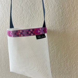 Puede incluir: Bolsa de malla blanca con un ribete de tela estampado en rosa y azul. La bolsa tiene una correa negra y el texto "Alhambra Goods" está impreso en el ribete de tela.