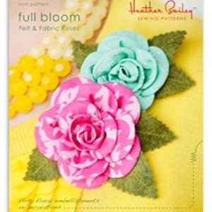 May include: Full Bloom sewing pattern for felt and fabric roses. The pattern cover features two roses, one pink with a white floral print and one teal blue. Both roses have green leaves.