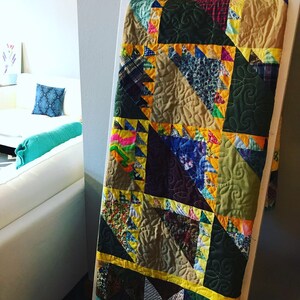May include: A patchwork quilt with a variety of fabrics in shades of brown, green, yellow, and blue. The quilt is made up of triangles and squares, and the edges are trimmed with yellow fabric.
