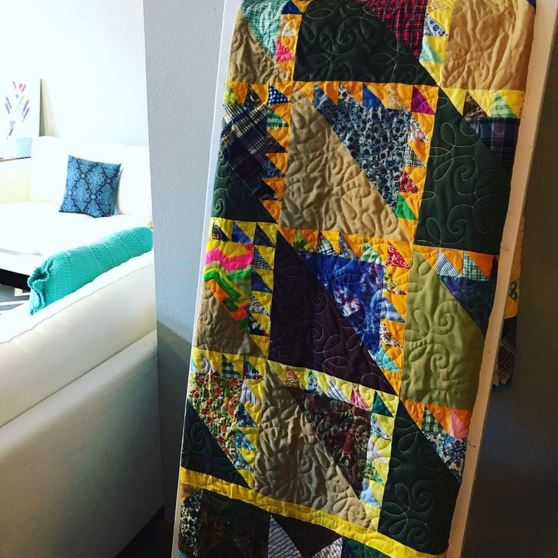 May include: A patchwork quilt with a variety of fabrics in shades of brown, green, yellow, and blue. The quilt is made up of triangles and squares, and the edges are trimmed with yellow fabric.