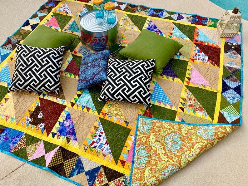 May include: A patchwork quilt with a variety of colors and patterns, including green, brown, yellow, blue, and pink. The quilt is made of squares and triangles, and it has a scalloped edge. There are four pillows on the quilt, two green, one black and white, and one blue. A metal bucket with the word "Coca-Cola" on it is in the background.